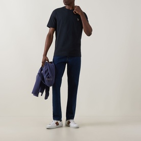 Model wearing Paul Smith blue cotton crew neck T-shirt with navy trousers and white trainers, carrying a navy jacket