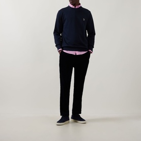 Model wearing Paul Smith blue crew neck sweatshirt with pink shirt, styled with black trousers and navy slip-on shoes.
