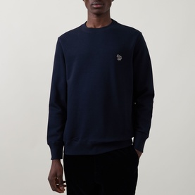 Model wearing Paul Smith blue crew neck sweatshirt with zebra logo patch on chest, styled with black trousers.