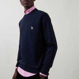 Model wearing Paul Smith blue crew neck sweatshirt with zebra logo patch, styled with a pink gingham shirt underneath.