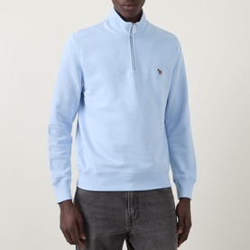 Model wearing Paul Smith Zebra Logo Half-Zip Sweatshirt in blue, with funnel neck and multicoloured zebra logo patch. Styled with grey trousers.