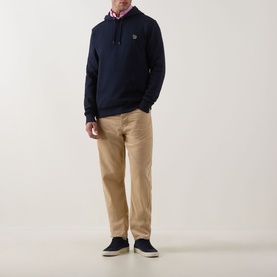 Model wearing Paul Smith Zebra Logo Hoodie in blue with beige chinos and navy trainers, pink shirt collar visible at neckline.