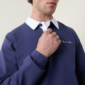 Model wearing Paul Smith blue cotton polo sweat with white collar, embroidered logo at chest, styled close-up shot