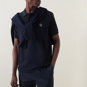 Model wearing Paul Smith Zebra Polo Shirt in blue piqu&eacute; cotton with zebra logo badge, paired with navy trousers and jacket draped over shoulders.