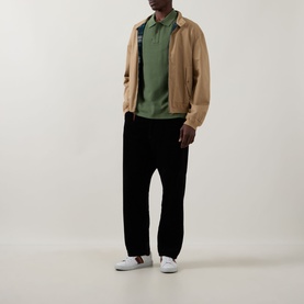 Model wearing Paul Smith green cotton polo shirt, styled with tan zip jacket, black trousers and white trainers.