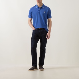 Model wearing Paul Smith blue cotton polo shirt with white tipped collar, styled with dark navy jeans and grey suede shoes.