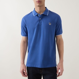 Model wearing Paul Smith blue cotton polo shirt with white tipped collar, zebra logo patch, and short sleeves, styled with dark jeans