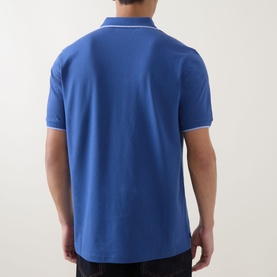 Model wearing Paul Smith blue cotton polo shirt, rear view, with white tipping detail on collar and cuffs
