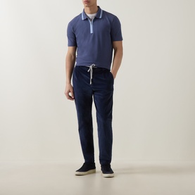 Model wearing Paul Smith blue cotton polo shirt with contrast tipped collar, styled with navy drawstring trousers and dark trainers.