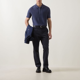 Model wearing Paul Smith blue cotton polo shirt with zip neck, styled with navy trousers and black loafers, holding a navy jacket.