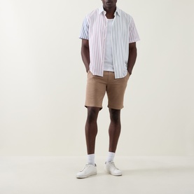 Model wearing Paul Smith Regular Fit Twill Chino Shorts in brown, styled with a striped short-sleeve shirt and white trainers.