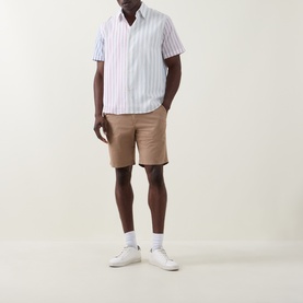 Model wearing Paul Smith Regular Fit Twill Chino Shorts in brown with white striped short-sleeve shirt and white trainers.