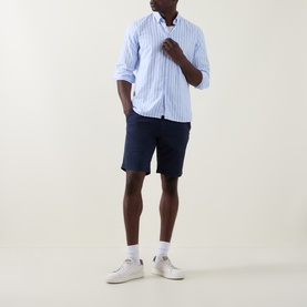 Model wearing Paul Smith Regular Fit Twill Chino Shorts in blue, styled with a light blue striped shirt and white trainers.