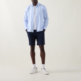 Model wearing Paul Smith Regular Fit Twill Chino Shorts in blue, styled with a light blue striped shirt and white trainers.