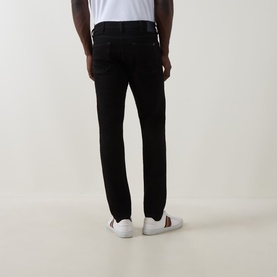 Model wearing Paul Smith Logo Tapered Jeans in blue, slim tapered cut, five-pocket style, styled with white trainers, rear view.
