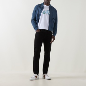 Model wearing Paul Smith Logo Tapered Jeans in blue, styled with a blue zip-up jacket, white graphic tee and white trainers.