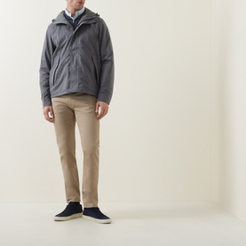 Model wearing Paul Smith Slim Tapered Jeans in brown, styled with a grey hooded jacket and navy canvas shoes.
