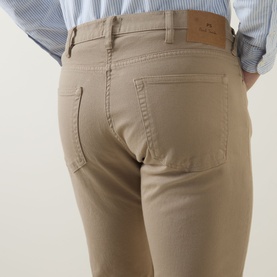 Model wearing Paul Smith Slim Tapered Jeans in brown, showing rear five-pocket detail with leather logo patch, styled with a blue striped shirt.