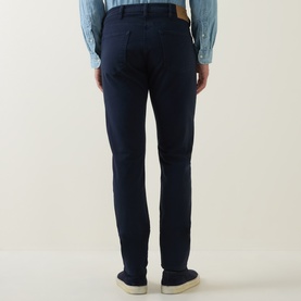 Model wearing Paul Smith blue slim-fit jeans, rear view, styled with a light blue chambray shirt and white trainers.