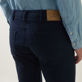 Model wearing Paul Smith blue slim jeans, rear view showing back pockets and branded leather patch, styled with a light blue chambray shirt.