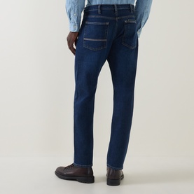 Model wearing Paul Smith blue straight-leg jeans, rear view, styled with a light blue shirt and dark brown leather loafers.