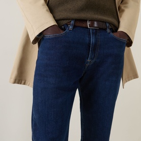 Model wearing Paul Smith blue straight-leg jeans with brown leather belt, styled with a beige jacket. Cropped waist-down view.