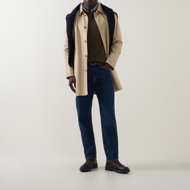Model wearing Paul Smith blue straight jeans with beige overcoat, olive jumper, and dark brown leather shoes.