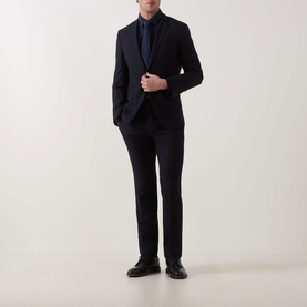 Model wearing Calvin Klein Slid Stretch Shirt in Dark Sapphire, styled with navy suit, tie, and black leather shoes.