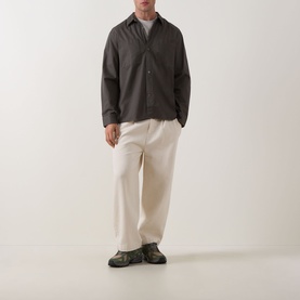 Model wearing Calvin Klein Garment Wash Twill Shirt in Beluga, dark grey, with cream wide-leg trousers and dark chunky shoes.