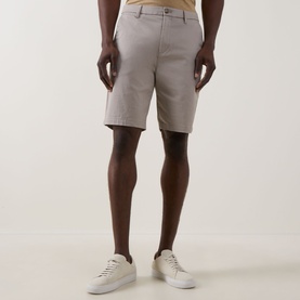 Model wearing light grey chino shorts with a flat front, styled with white leather trainers