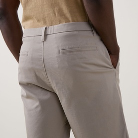 Model wearing light grey slim-fit chino trousers, rear view showing back pocket detail, styled with a beige top