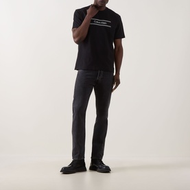 Model wearing Calvin Klein 20S SPW Graphic Logo T-Shirt in black with contrast chest logo, styled with dark grey jeans and black shoes.