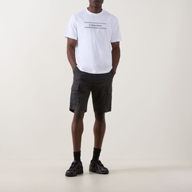 Model wearing Calvin Klein 20S SPW Graphic Logo T-Shirt in Bright White with dark cargo shorts and black trainers.