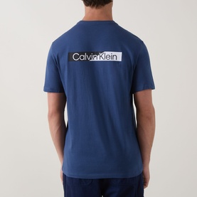 Model wearing Calvin Klein 30S Graphic Logo T-Shirt in Dark Denim, rear view showing white box logo print on back.