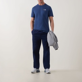 Model wearing Calvin Klein 30S Graphic Logo T-Shirt in Dark Denim with navy trousers, carrying a grey jacket, wearing silver trainers.
