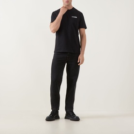Model wearing Calvin Klein 30S Graphic Logo T-Shirt in black with crew neck, styled with black trousers and chunky leather shoes.