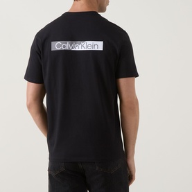 Model wearing Calvin Klein 30S Graphic Logo T-Shirt in black, rear view showing large logo print across back. Styled with dark jeans.