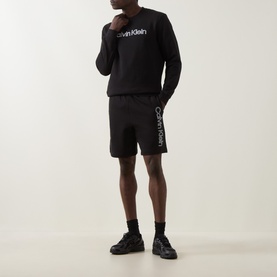 Model wearing Calvin Klein Black Crew Neck sweatshirt with matching black logo shorts, black socks and chunky black trainers.