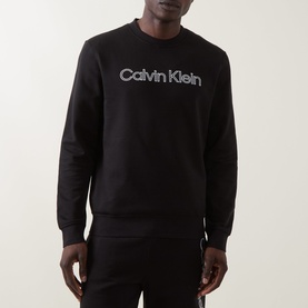 Model wearing Calvin Klein black cotton crew neck sweatshirt with tonal logo print, styled with matching black joggers.