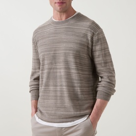 Model wearing Calvin Klein Tonal Slub Knitted Sweater in Roast Cashew, crew neck, long sleeves, ribbed trims, styled with white trousers.