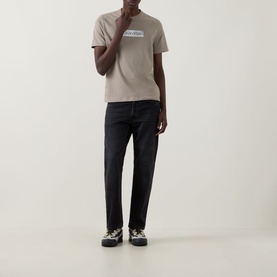 Model wearing Calvin Klein 30s Logo T-Shirt in Roast Cashew, crew neck, short sleeves, styled with dark trousers and chunky trainers.