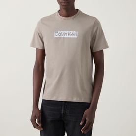 Model wearing Calvin Klein 30s Logo T-Shirt in Roast Cashew, crew neck, short sleeves, with contrast logo chest print. Styled with dark jeans.