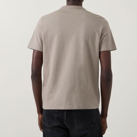 Model wearing Calvin Klein 30s Logo T-Shirt in Roast Cashew, rear view, crew neck, short sleeves, paired with dark jeans.