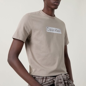 Model wearing Calvin Klein 30s Logo T-Shirt in Roast Cashew, crew neck, short sleeves, with checked trousers.