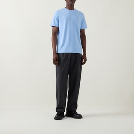 Model wearing Calvin Klein Monogram Logo T-Shirt in Placid Blue, crew neck, short sleeves, styled with dark wide-leg trousers and black shoes.