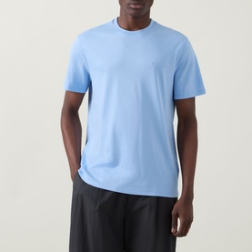 Model wearing Calvin Klein Monogram Logo T-Shirt in Placid Blue, crew neck with subtle chest logo embroidery, paired with black trousers.