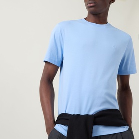 Model wearing Calvin Klein Monogram Logo T-Shirt in Placid Blue, crew neck, short sleeves, chest logo embroidery, styled with dark trousers.