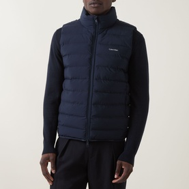 Model wearing Calvin Klein Lightweight Quilted Gilet in Dark Sapphire, quilted finish, high neck, two-way zip, styled with navy knitwear and joggers