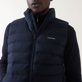 Model wearing Calvin Klein Lightweight Quilted Gilet in Dark Sapphire, high neck, two-way zip, quilted finish, styled over navy long-sleeve top.
