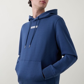 Model wearing Calvin Klein Dark Denim hoodie with kangaroo pocket, drawstring hood, and small chest logo graphic.